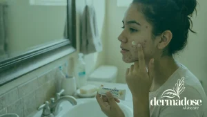 Chica joven con acné aplicando crema de azufre en la mejilla frente al espejo del baño