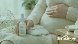 Mujer embarazada sosteniendo el sérum The Ordinary Hyaluronic Acid 2% + B5 junto a zapatitos de bebé blancos, ilustrando la seguridad del ácido hialurónico en el embarazo