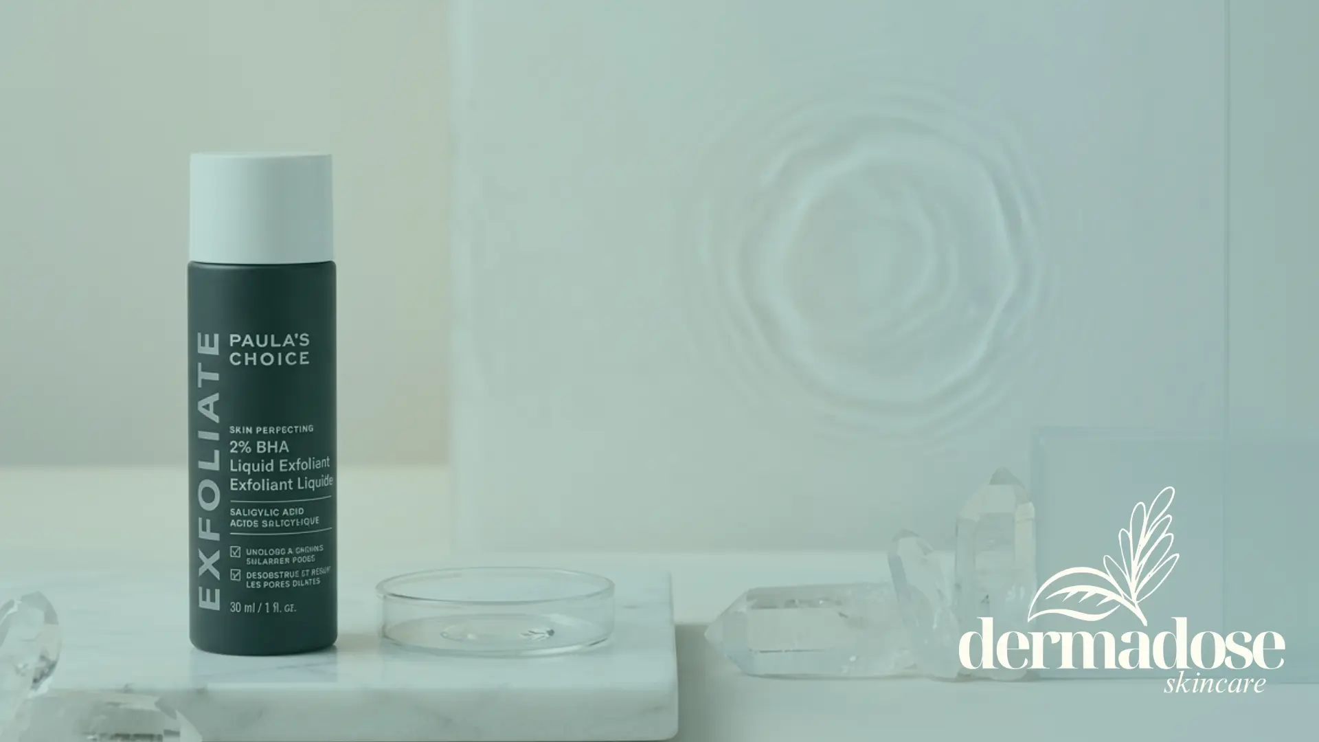 Paula's Choice Skin Perfecting 2% BHA Liquid Exfoliant botella verde oscura sobre superficie de mármol con cristales y placa de Petri