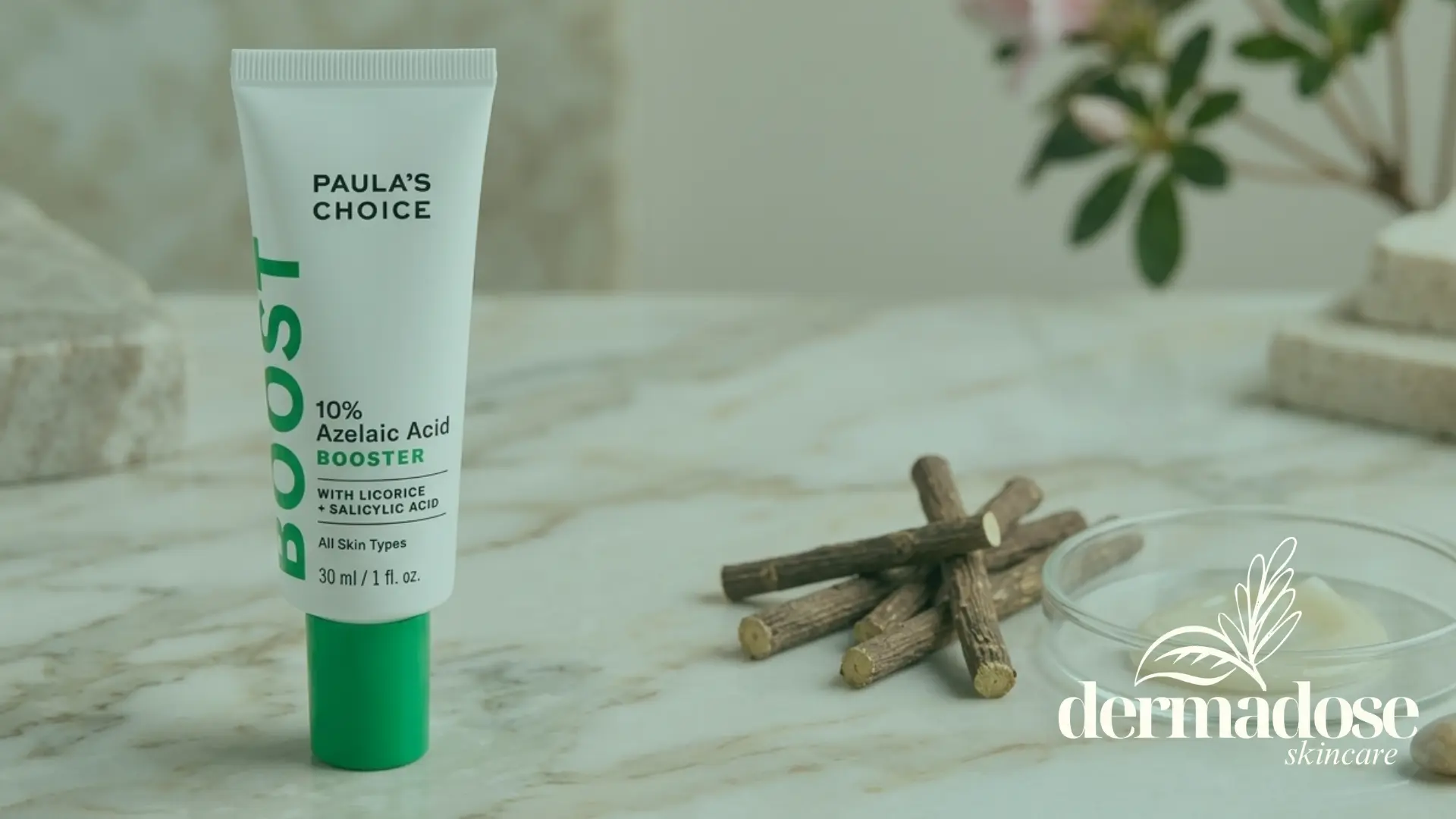 Paula's Choice 10% Azelaic Acid Booster tubo blanco con tapa verde sobre mármol junto a raíces de regaliz