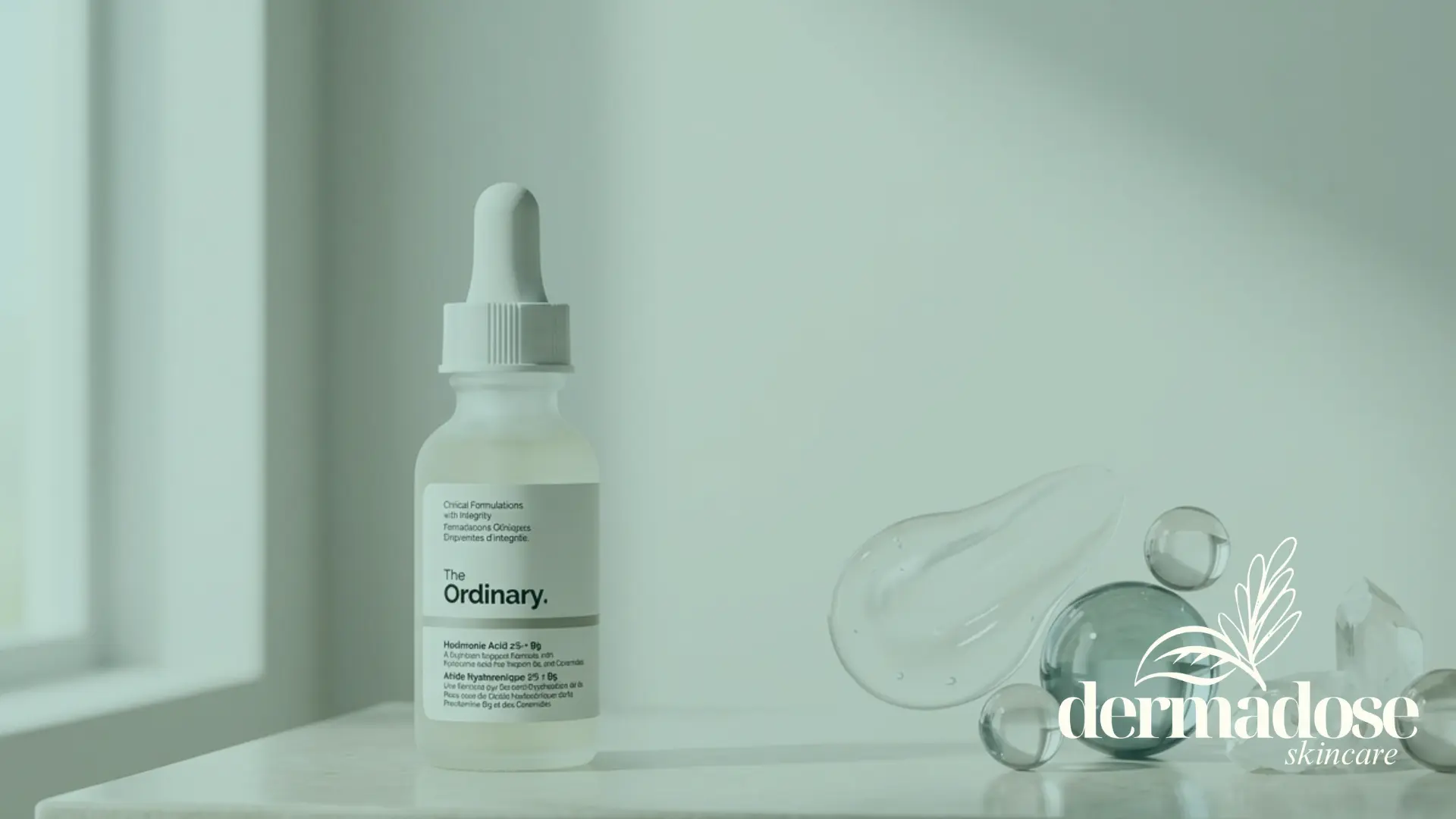 The Ordinary Hyaluronic Acid 2% + B5 frasco transparente con gotero sobre superficie de mármol con gotas de sérum y esferas de cristal